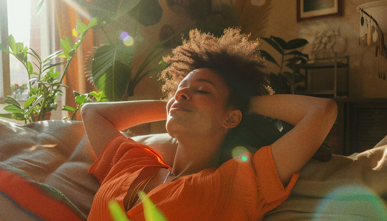 indica-strains | Kurvana | Curated for years. Experienced in moments. Woman relaxing on a sofa in a sunlit room with green plants, enjoying a peaceful moment.